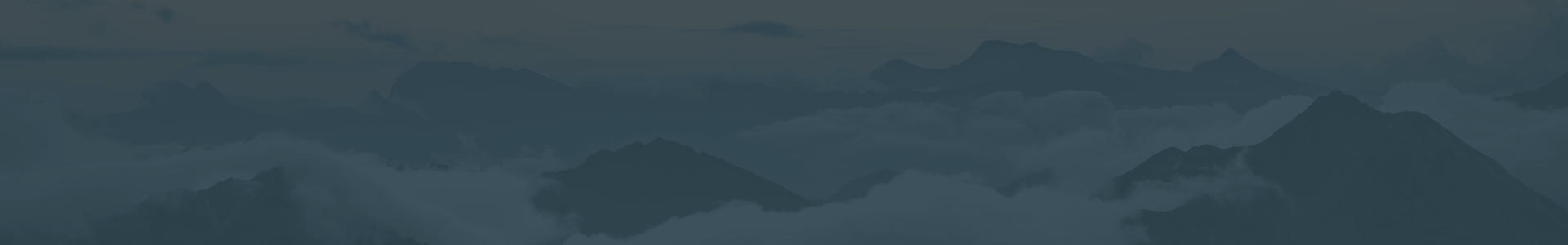 A landscape of layered mountain ranges, shrouded by clouds.